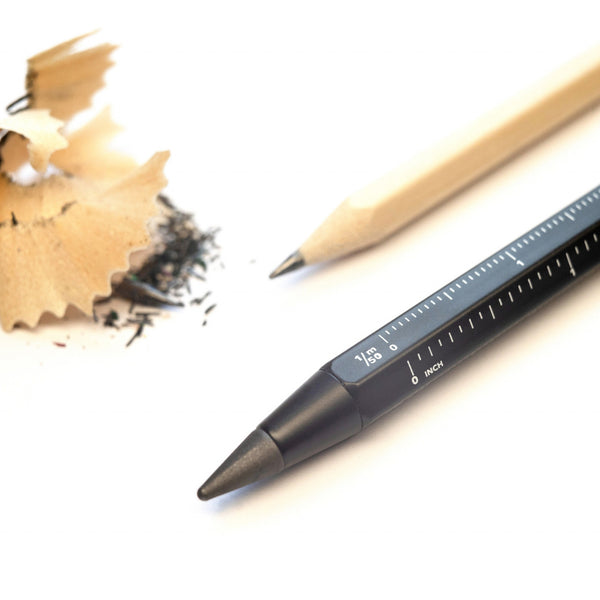 Auf einer weißen Fläche liegen ein angespitzter Bleistift, Bleistiftspäne und ein schwarzer Multitasking-Bleistift mit Lineal.