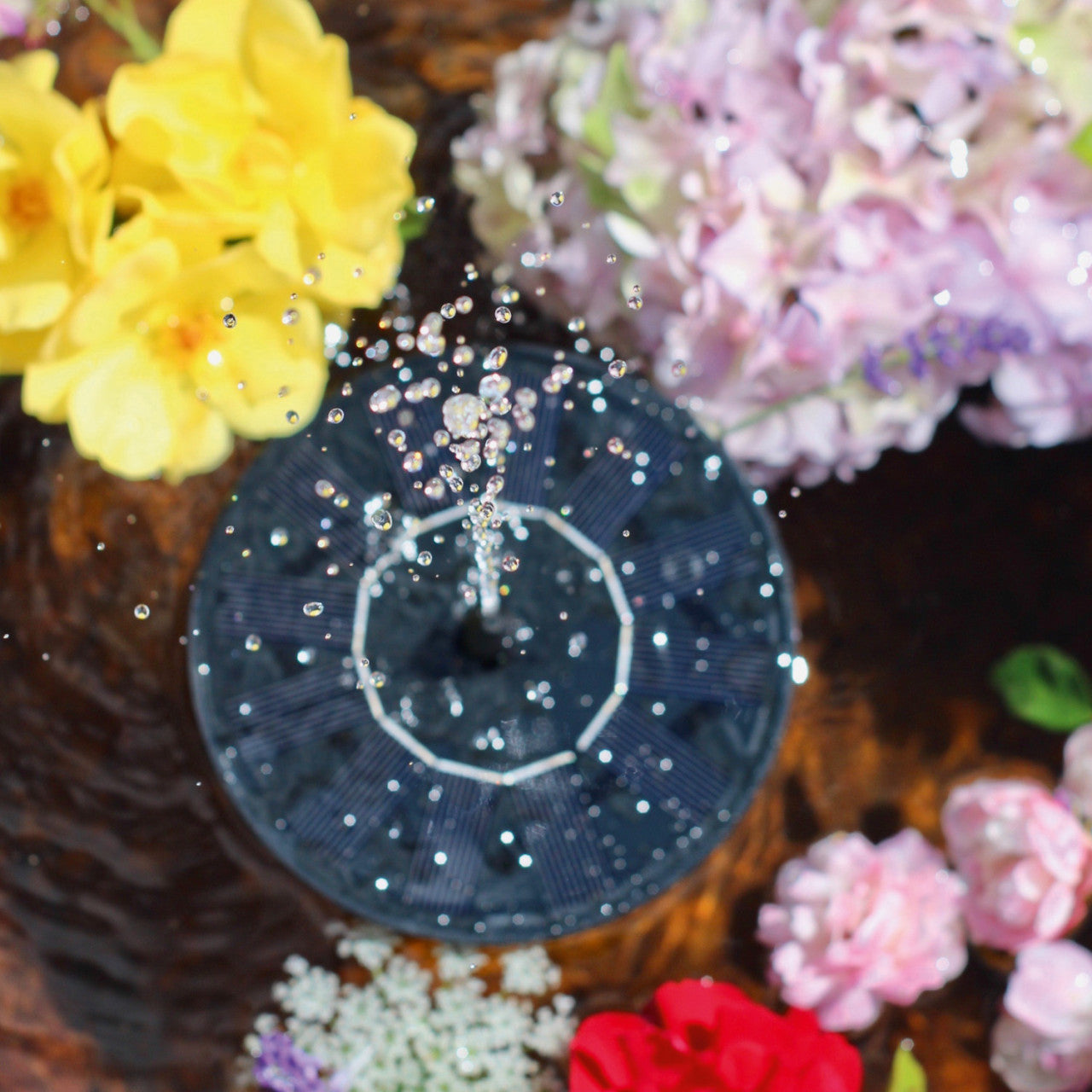 Solar-Brunnen sprüht Wasser, umgeben von leuchtenden gelben, rosa und roten Blumen – ein bezauberndes Gartendeko-Wasserspiel für stilvolle Akzente im Garten.