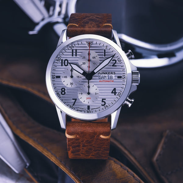 Eine silberne Junkers Aviator Automatik-Armbanduhr mit braunem Lederarmband, Tages- und Datumsanzeige, verfügt über robuste Automatikwerk-Technologie.