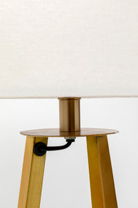 Nahaufnahme einer modernen Stehlampe mit dreibeinigem Holzfuß und einem Lampenschirm aus Leinen, die ihr skulpturales Design zur Schau stellt.