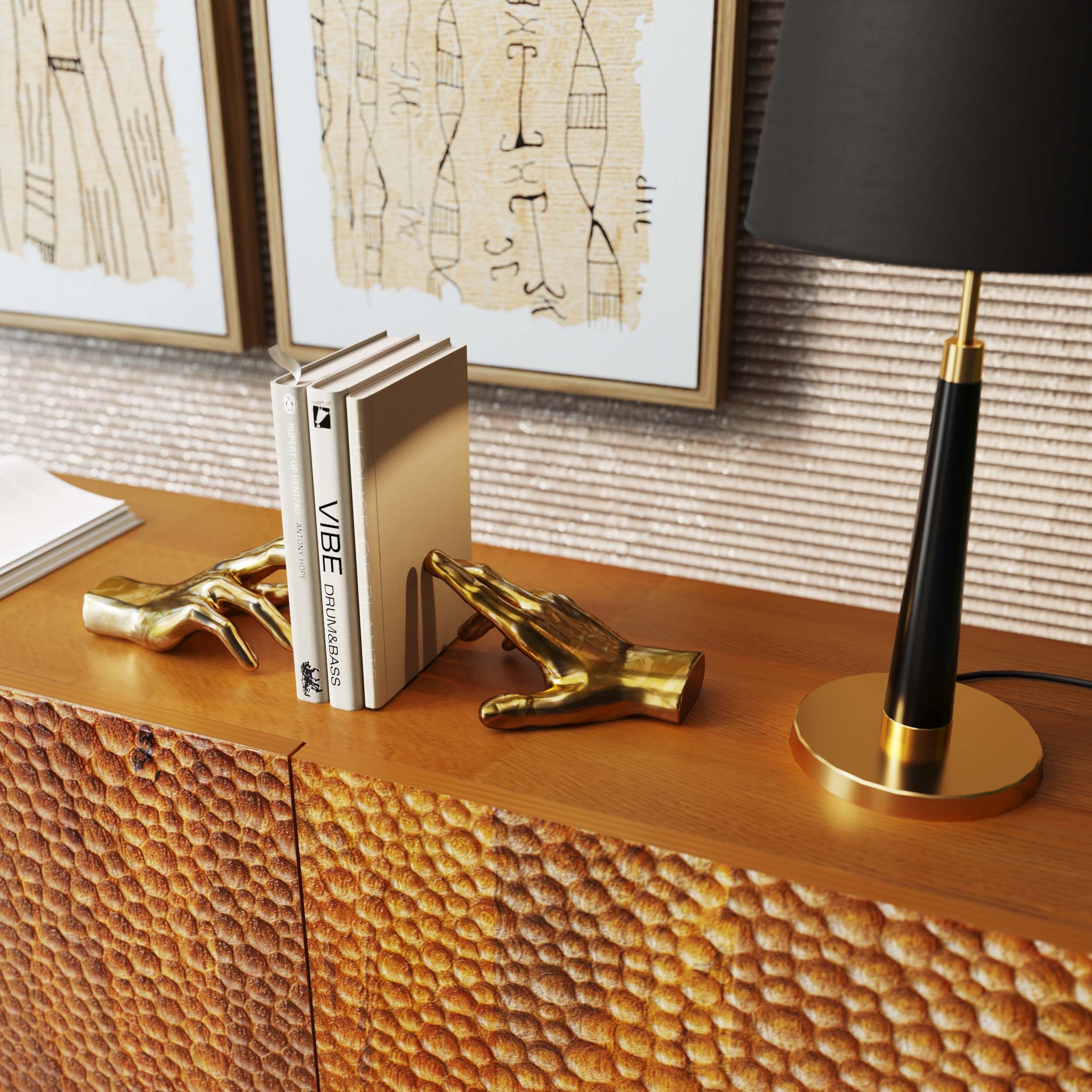 Goldene dekorative Hände aus Polyresin dienen als stilvolle Buchstütze und halten Bücher auf einem Holzschrank neben einer schwarz-goldenen Lampe und gerahmter Kunst.