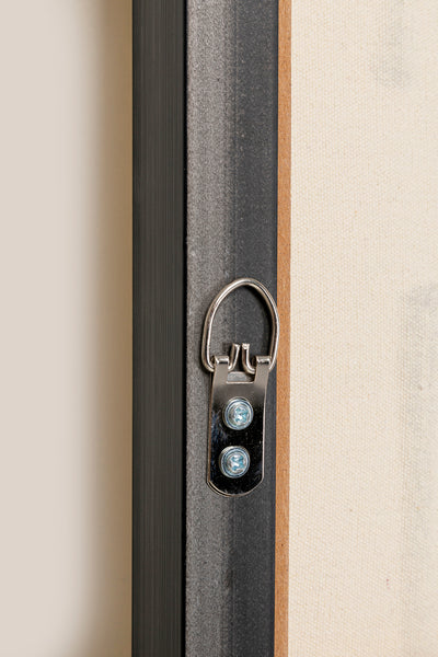 Nahaufnahme eines D-Ring-Aufhängers aus Metall, der mit zwei Schrauben an der Rückseite eines handgemalten Ölfarbe-Leinwandbilds in Schwarz Creme-Weiß befestigt ist.