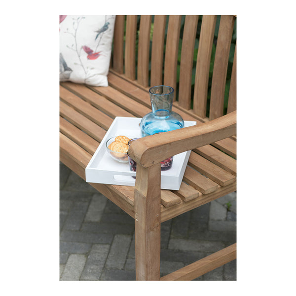 Eine Teakholzbank mit einem Tablett, auf dem sich ein blauer Glaskrug, eine Schüssel mit Keksen und ein Kissen mit Vogelaufdruck befinden, verleiht Ihrer Outdoor-Gestaltung Charme.