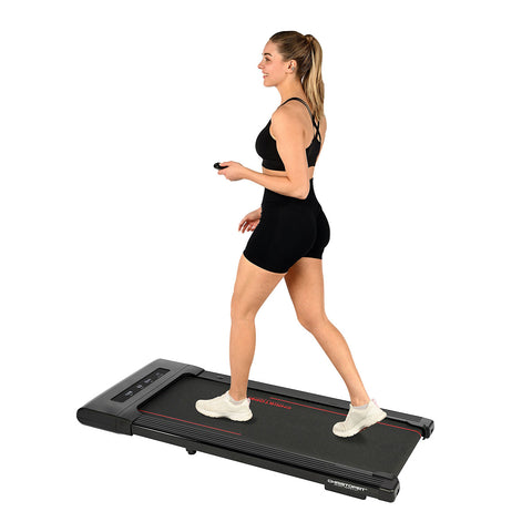 Eine Person in sportlicher Kleidung geht auf einem flachen Laufband  das auf weißem Hintergrund steht.

