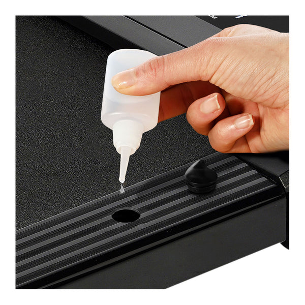 Eine Hand hält eine kleine Flasche  aus der Tropfen auf eine schwarze  geriffelte Oberfläche fallen.
