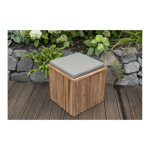 Auf dem Deck, umgeben von Steinen und üppigen grünen Pflanzen, steht ein Outdoor-Hocker Oxford aus Teakholz mit einem grauen Kissen.