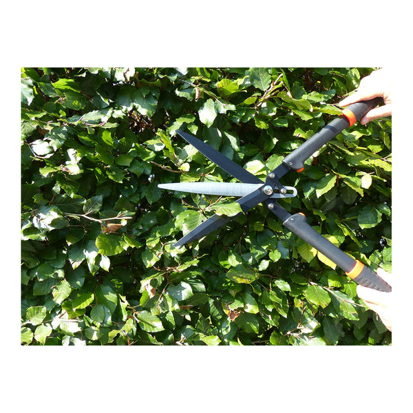 Eine Heckenschere schneidet eine dicht belaubte Hecke.