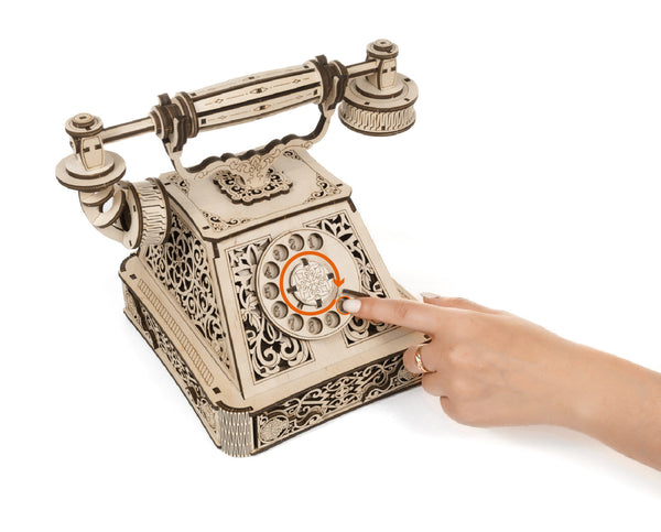Antikes Modelltelefon aus Holz mit detaillierten Verzierungen  bei dem eine Hand die Wählscheibe dreht.
