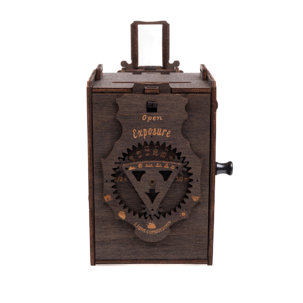Eine aus Holz gefertigte  rustikal wirkende Kamera mit sichtbarem Zahnradsystem auf der Vorderseite  auf dem "Open Exposure" und weitere Markierungen zu Belichtungszeiten stehen.
