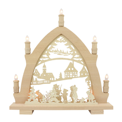 Ein hölzerner Schwibbogen mit ausgeschnittenen winterlichen Dorf- und Kinder-Szenen  geschmückt mit sieben elektrischen Kerzen  die eine warme Atmosphäre verbreiten.

