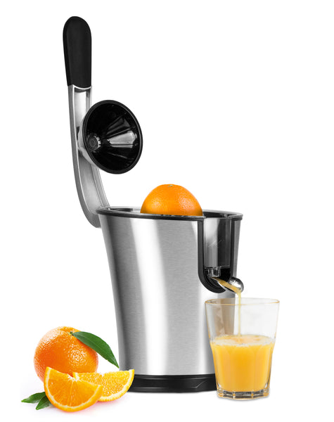 Eine silberne elektrische Saftpresse mit Hebel presst Orangen  neben der ein halbes Glas frischer Orangensaft und geschnittene Orangen liegen.
