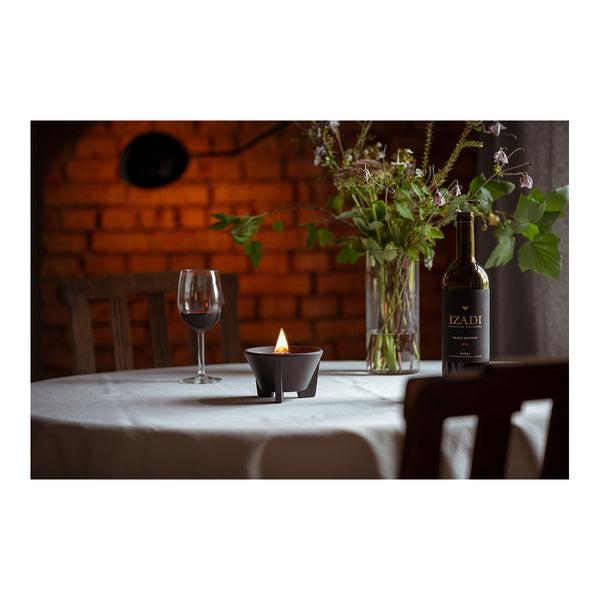 Ein gedeckter Tisch mit einem Glas Rotwein  einer brennenden Kerze und einem Blumenstrauß in einer Vase vor einer Ziegelwand.
