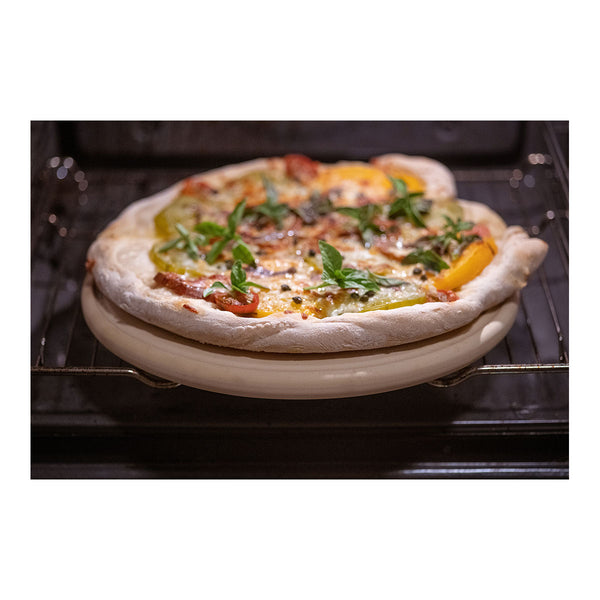 Eine selbstgemachte Pizza mit Tomaten  Basilikum und Kapern liegt auf einem Grillrost.
