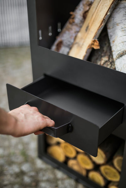 Eine Hand zieht an einer schwarzen Schublade eines Holzregals  das mit gestapeltem Holz gefüllt ist.
