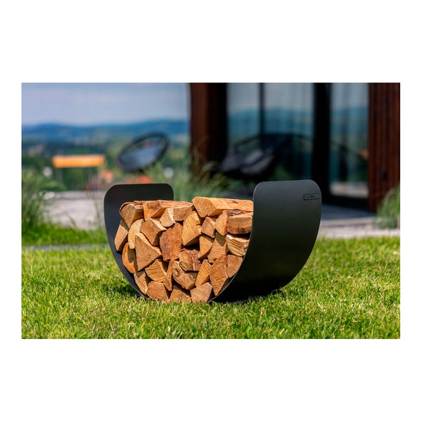 Ein modernes  halbmondförmiges  schwarzes Holzgestell steht auf einem Rasen. Im Hintergrund unscharf ist ein Haus und ein Stuhl