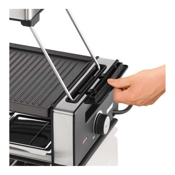 Eine Hand bedient den Deckel eines elektrischen Kontaktgrills mit gerippter Grillfläche und Drehknopf auf der Vorderseite.
