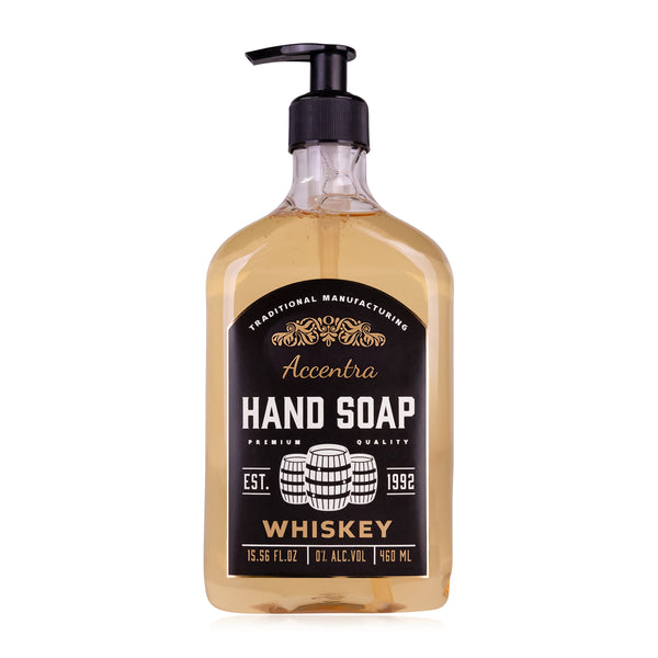 Eine durchsichtige Pumpflasche mit bernsteinfarbener Flüssigkeit enthält "Accentra Hand Soap" mit Whiskeyduft und schwarzem Etikett mit goldenen Verzierungen.
