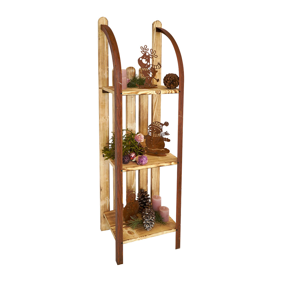Ein dekoratives Regal in Form eines historischen Holzschlittens  das mit kleinen Metallfiguren  grünen Zweigen  Zapfen und rosa Kerzen geschmückt ist.

