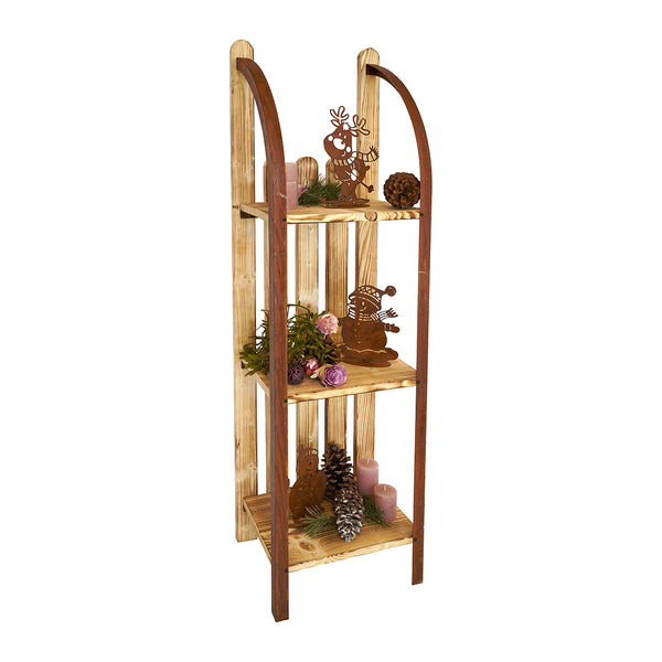 Ein dekoratives Regal in Form eines historischen Holzschlittens  das mit kleinen Metallfiguren  grünen Zweigen  Zapfen und rosa Kerzen geschmückt ist.
