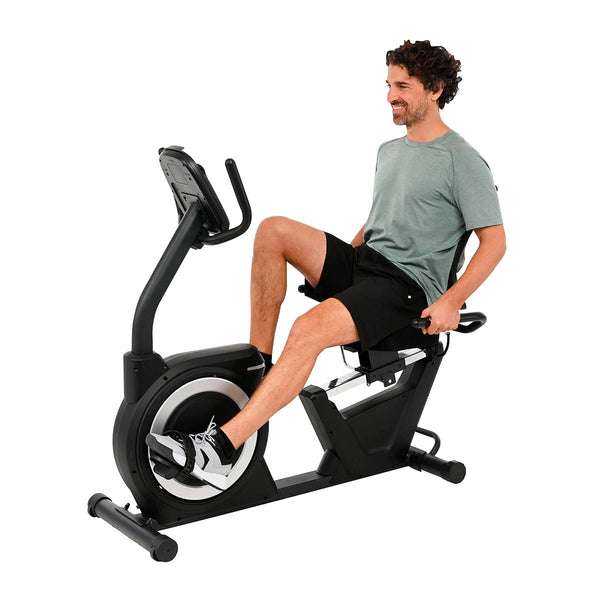 iegeergometer vor weißem Hintergrund, mit komfortablem Sitz, Pedalen und übersichtlichem Display für gesundheitsbewusstes Ausdauertraining zu Hause mit Mann in Sportklamotten, der es nutzt. Abbildung von vorne.