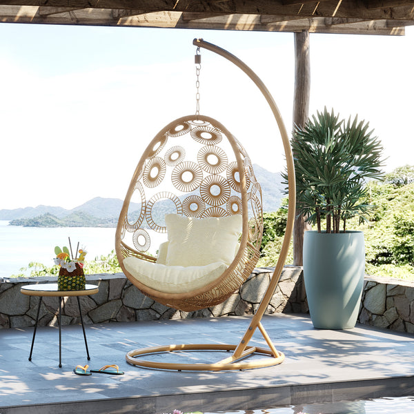 Schicker Hängesessel aus Poly-Rattan mit weichen Kissen auf einer Terrasse, Meer und Berge im Hintergrund, Topfpflanze trägt zum Boho-Style-Ambiente bei.
