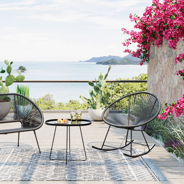 Außenterrasse mit modernen Stühlen im Acapulco-Design, einem Tisch mit Getränken, Meerblick, Kakteen und rosa Blumen an einem sonnigen Tag.