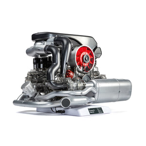 Ein detailliertes, freiliegendes Porsche 911 Turbo-Motormodell mit sichtbaren Rohren, Lüfter und Komponenten auf einer weißen Basis – präsentiert Turbotechnologie in ihrer besten Form in diesem Meisterwerk des Hochleistungssportwagens.