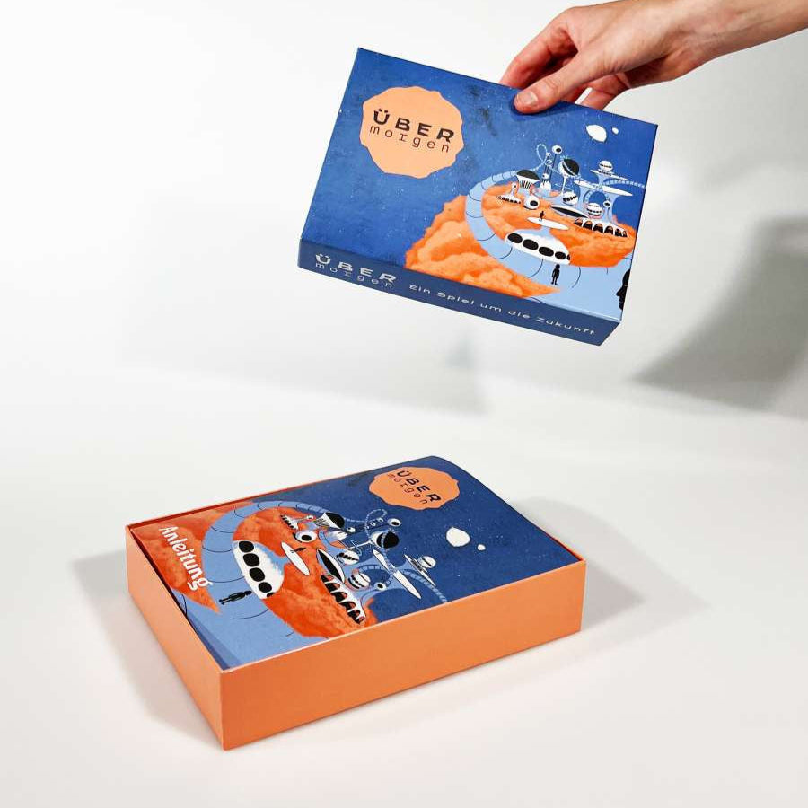 Eine Hand hebt eine blau-orangefarbene Gesellschaftsspiel-Box mit abstrakten Illustrationen und dem Text ÜBER morgen – perfekt für Weltraumreisende, die den verlassenen Planeten erkunden.