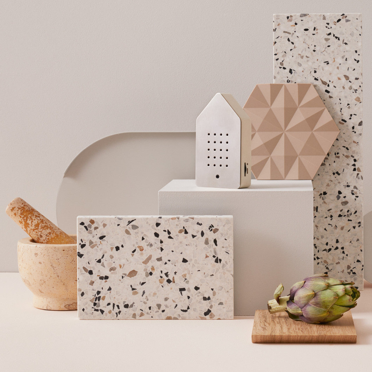 Eine Terrazzofliese, ein Mörser mit Stößel, eine Artischocke und geometrische Formen auf einem neutralen Hintergrund rufen ruhige Entspannung hervor – wie ein visuelles Vogelkonzert für Ihre Sinne.