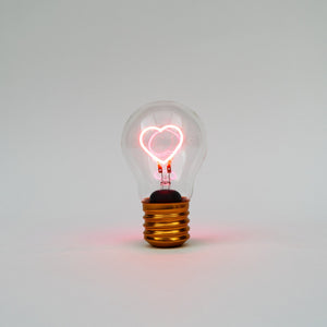 Klare Edison-Glühbirne mit leuchtendem herzförmigen Glühfaden vor einem schlichten weißen Hintergrund.