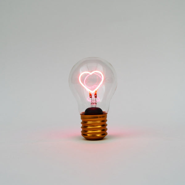 Klare Edison-Glühbirne mit leuchtendem herzförmigen Glühfaden vor einem schlichten weißen Hintergrund.