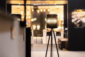 Eine moderne Stativlampe leuchtet vor einem stilvollen, warm beleuchteten Interieur mit flauschigen Möbeln und ambienter LED-Beleuchtung und schafft eine gemütliche, einladende Atmosphäre.