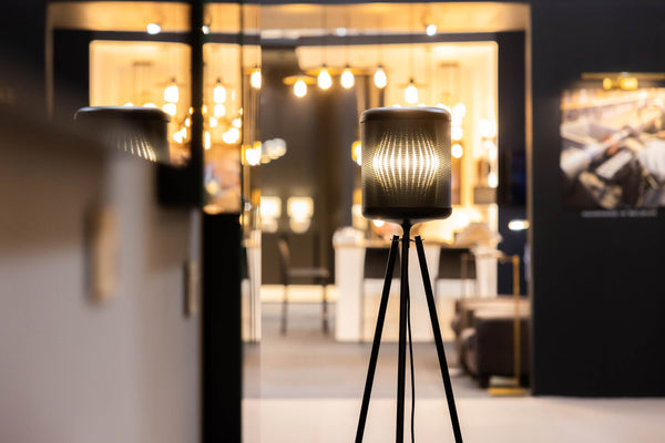 Eine moderne Stativlampe leuchtet vor einem stilvollen, warm beleuchteten Interieur mit flauschigen Möbeln und ambienter LED-Beleuchtung und schafft eine gemütliche, einladende Atmosphäre.