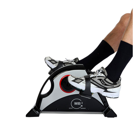 Eine Person benutzt ein Mini-Heimtrainer-Pedalgerät  ihre Füße sind mit Turnschuhen und schwarzen Socken auf den Pedalen befestigt.
