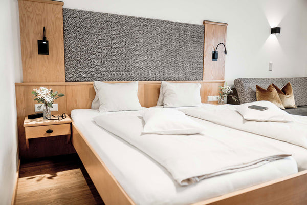 Hotelzimmerbett mit Blumenvase und Brille auf dem Nachttisch 