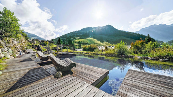 Teich mit Holzsitzmöglichkeiten in den Bergen. Die Sonne scheint, die Natur ist grün.