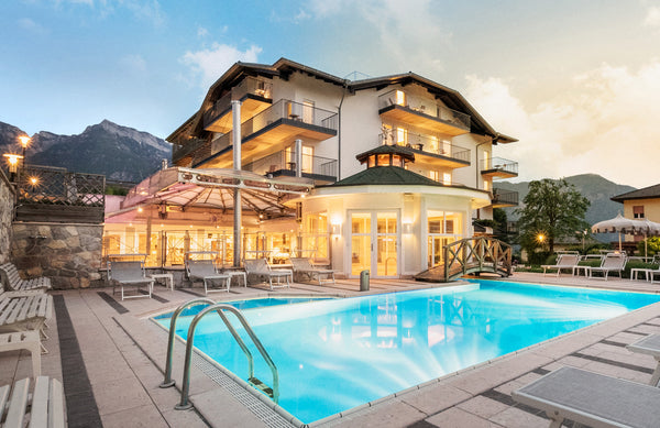 Hotelanlage in den Bergen bei Abenddämmerung. Vor dem Hotel ist ein Pool mit Liegestühlen drumherum.