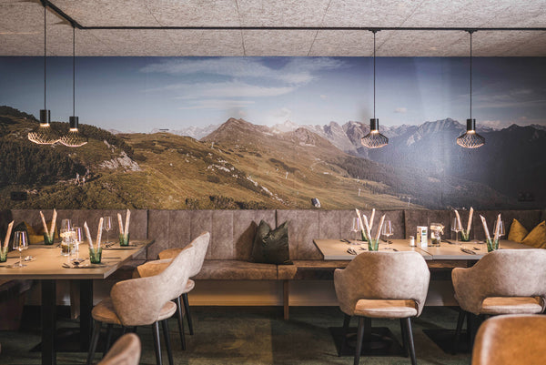 Restaurant mit gedeckten Tischen vor einem großen Bild auf dem eine Fotografie von Bergen abgebildet ist.