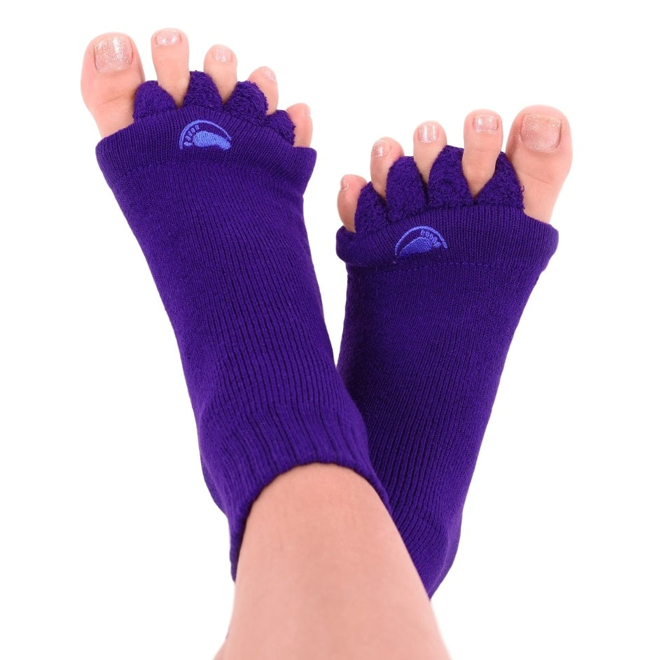 Eine Person, die lila Fußausrichtungssocken trägt, legt ihre Füße darauf. Diese für ihren Komfort bekannten Socken trennen jeden Zeh, und die Zehennägel sind mit einem schimmernden hellrosa Lack lackiert.