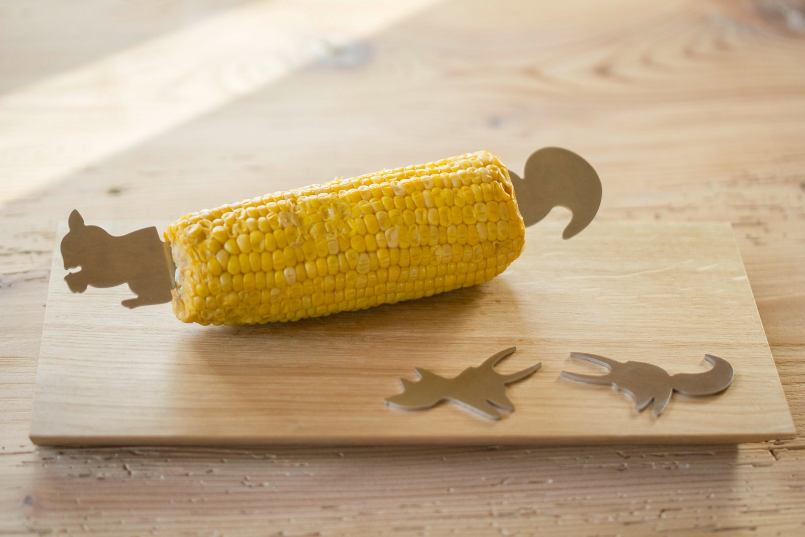 Maiskolben mit Maiskolbenhalter aus Edelstahl Häschen auf einem Brett.