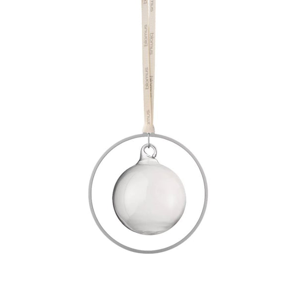 Klare Glaskugel als Ornament hängt in einem Metallring in Messingoptik an einem Band mit Text, vor weißem Hintergrund.