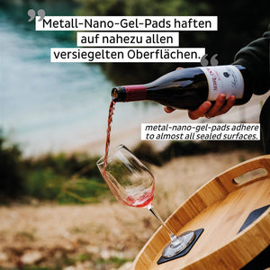 Eine Person gießt Rotwein in Kristallgläser auf einem Tablett im Freien in der Nähe von Wasser, mit Werbetext überlagert.