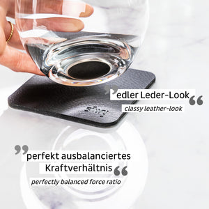 Eine Hand stellt ein Glas auf einen Untersetzer in schwarzer Lederoptik auf einer weißen Marmoroberfläche und unterstreicht so die nachhaltige Spitzenqualität in jedem Detail.