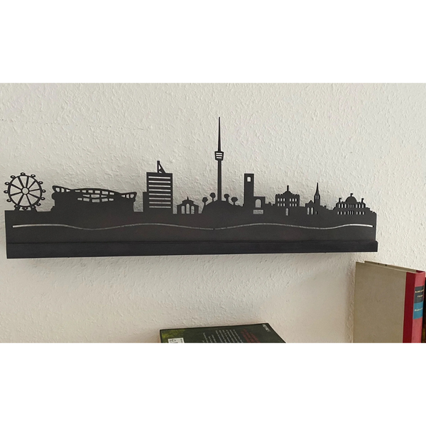 Schwarzes Skyline-Silhouettendekor aus Metall an einer weißen Wand über Büchern, mit Gebäuden und einem Riesenrad, wunderschön akzentuiert mit LED-Lichtern für einen modernen Touch.
