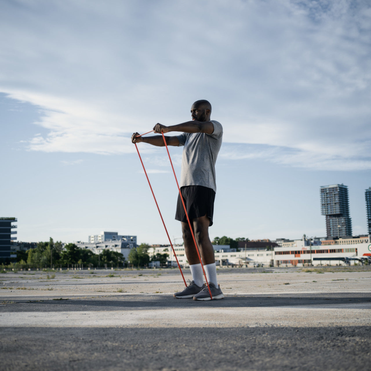 Mann trainiert im Freien mit einem STRAFFR Training-Fitnessband, streckt die Arme, während im Hintergrund die Stadtgebäude aufragen, und nutzt das Smartes Tracking für optimale Leistung.