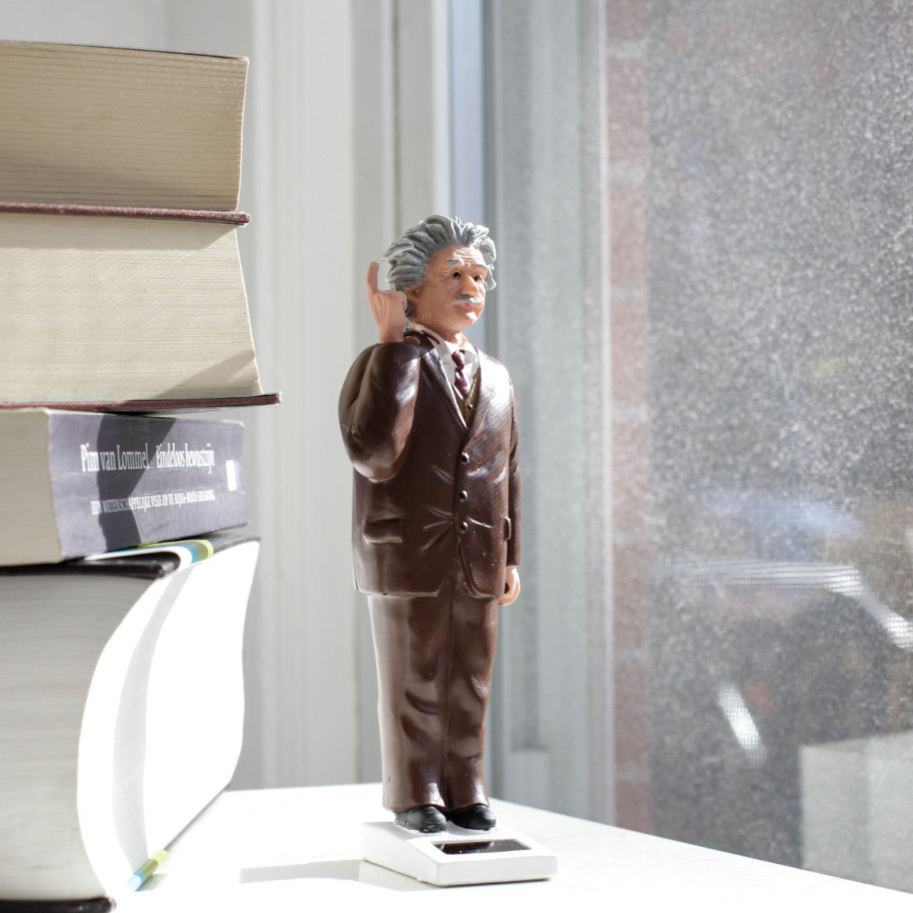 Eine kleine Solar-Einstein-Figur im Anzug steht neben gestapelten Büchern an einem sonnigen Fenster – perfekt für Fans sammelbarer Figuren.