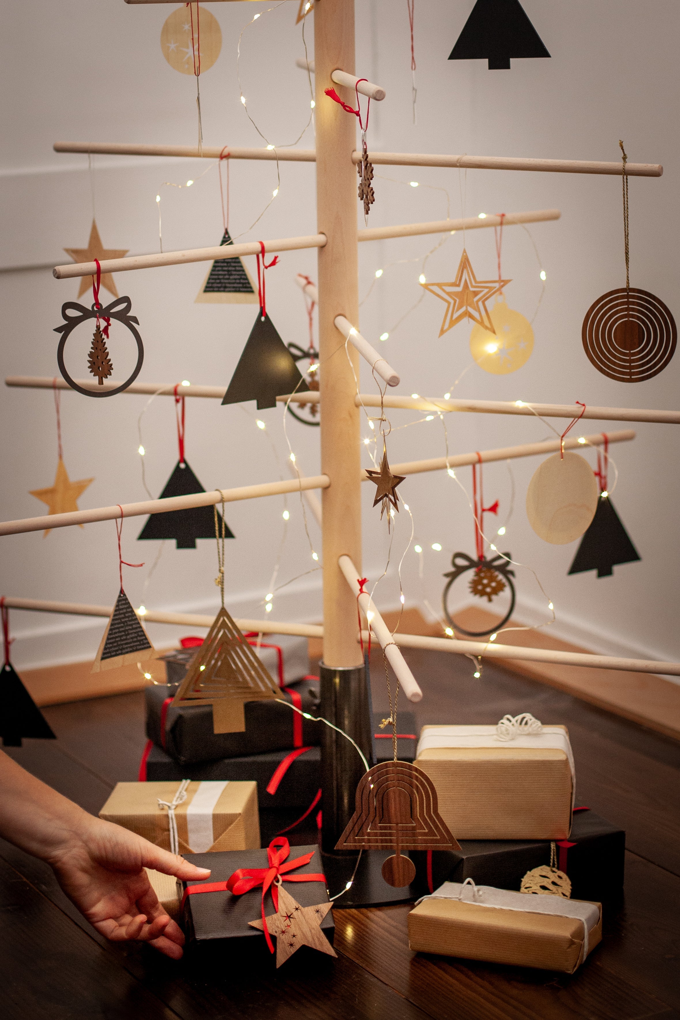 Minimalistischer abstrakter Baum aus Buchenholz mit geometrischen Ornamenten, nachhaltige Weihnachtsbäume präsentieren Geschenke, während eine Hand nach einem davon greift.