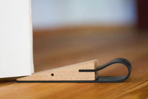 Der Holztürstopper STOPPERMAUS verfügt über ein schwarzes Gummiende und hält eine weiße Tür auf einem Holzboden offen – ein eleganter Design-Türstopper in charmanter Mäuschen-Form.