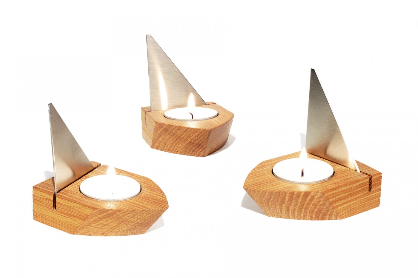 Drei hölzerne Teelichthalter aus Eichenholz mit dreieckigen Edelstahlsegeln, die an kleine Segelboot-Windlichter erinnern.