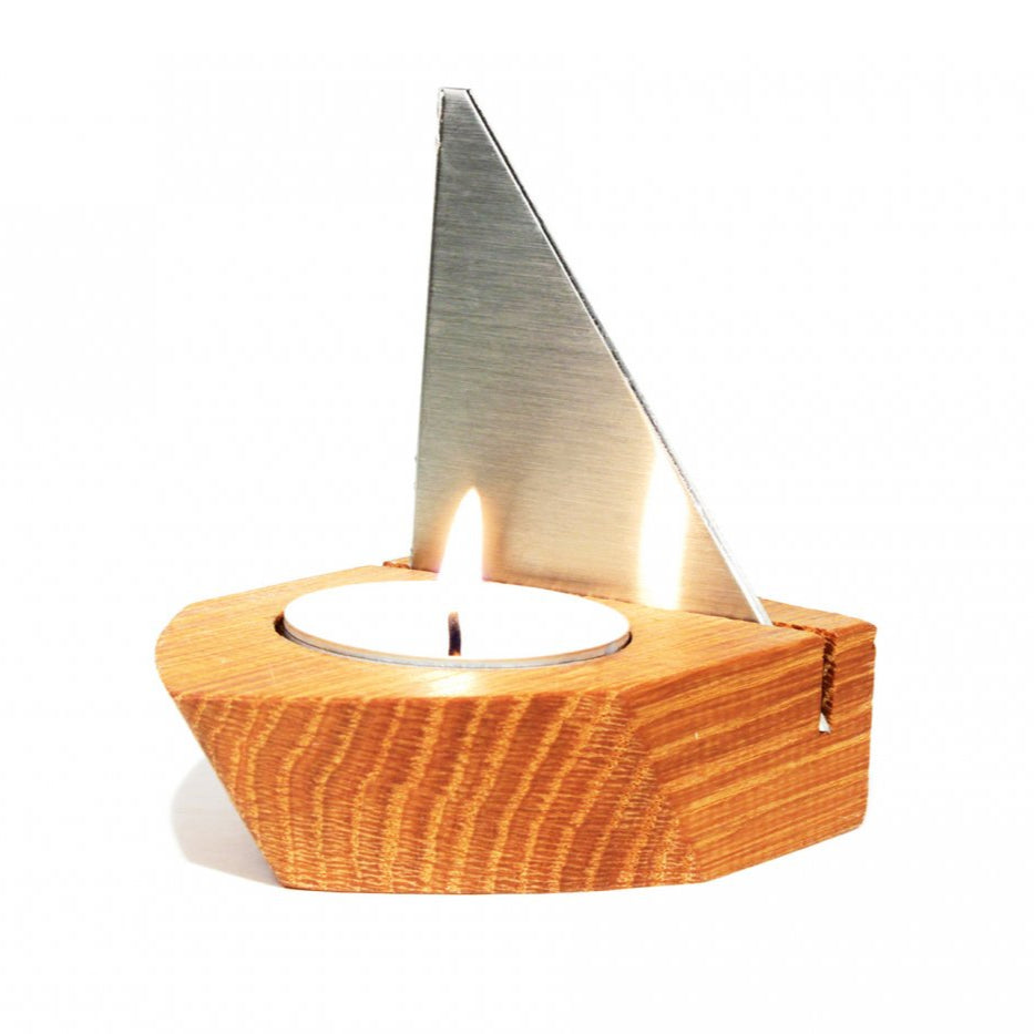 Ein aus Eichenholz gefertigter Kerzenhalter besteht aus einem eleganten, segelartigen Edelstahlteil, das ein brennendes Teelicht hält – ein elegantes Windlicht für jede Umgebung.